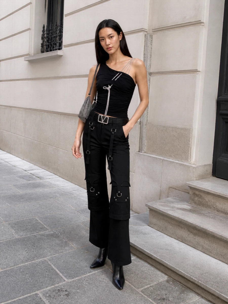This look builds on the top’s asymmetric, crystal-strapped drama with sharp black harness cargos and a cinched, glittering waist, creating a long, lean line that feels equal parts street and club. Pointed black stilettos keep everything sleek and elevated, while a crystal-dripped mini baguette locks in the black-and-silver, after-dark Y2K energy. It’s a confident FW night-out uniform that reads designer from every angle without ever feeling overworked.