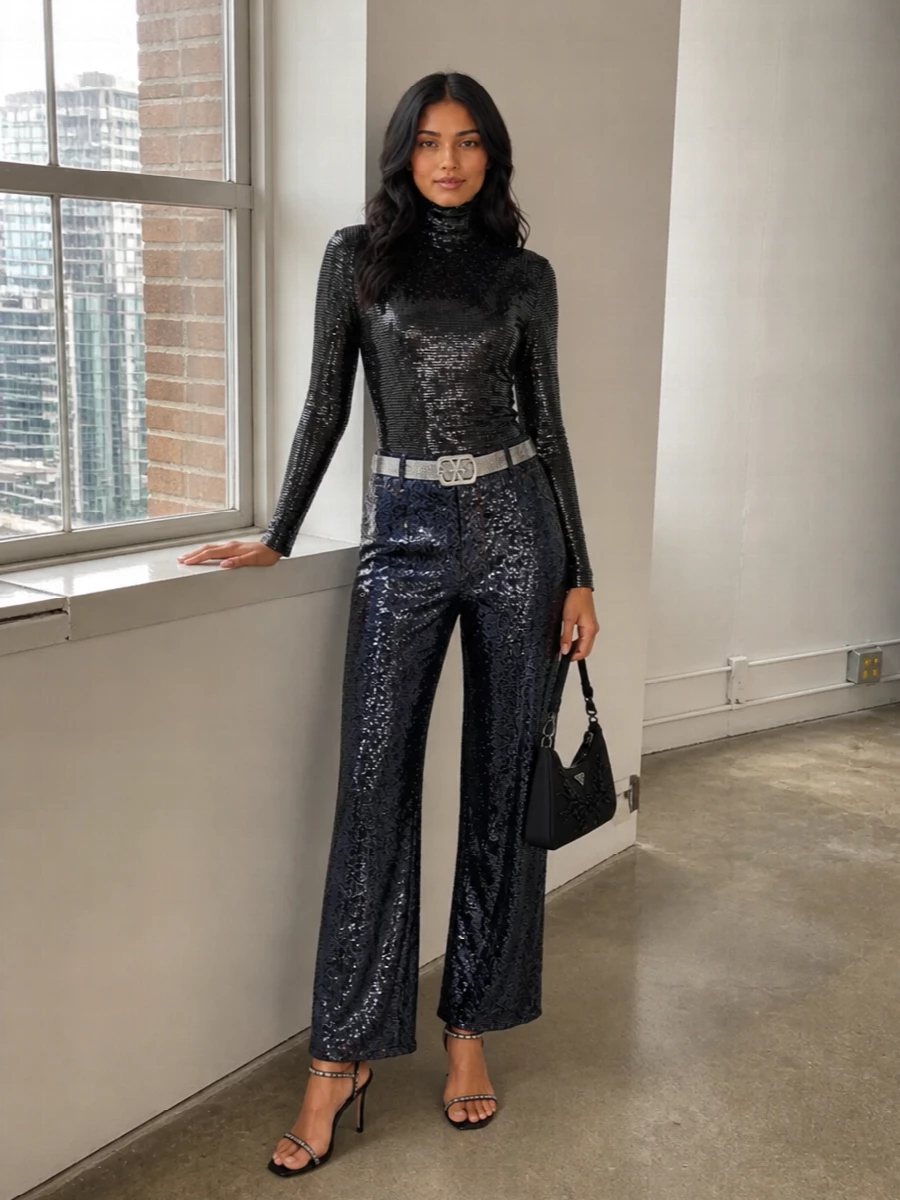 High-shine midnight trousers meet a second-skin sequinned turtleneck for a long, lean take on night-out dressing that still feels sharply composed. Crystal-strapped stilettos, a beaded black baguette and a mirrored belt concentrate the metal accents so the whole outfit glows in a deep, inky palette rather than screaming for attention. It is a confident, city-after-dark uniform built on clean lines and intentional sparkle placement.