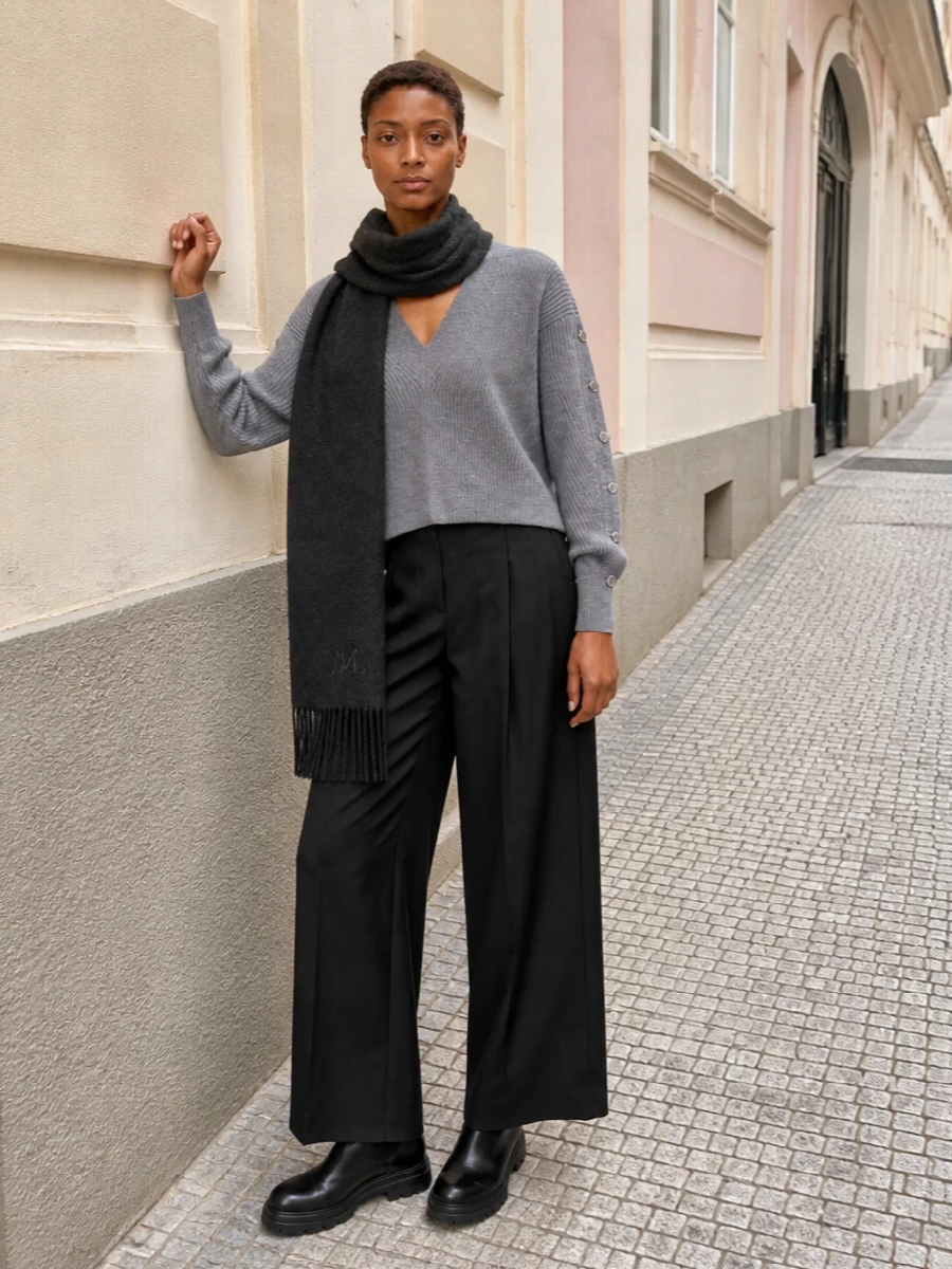 A cropped grey knit pairs with high-waisted black wide-leg trousers for a clean, elongated silhouette that feels soft yet sharply pulled together. Chunky black ankle boots ground the volume, while a structured charcoal top-handle and tonal scarf keep the palette cool and composed for city days and discreet dinners alike.