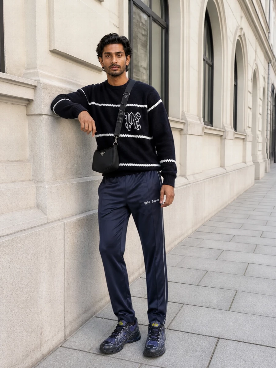 Ink navy track pants meet a striped Palm Angels knit for a tight, athletic palette that still feels considered. Tonal technical runners and a compact Prada crossbody keep the lines clean and city ready, with a discreet belt giving just enough hardware at the waist. It is an easy uniform for late days that roll into night without needing a change.