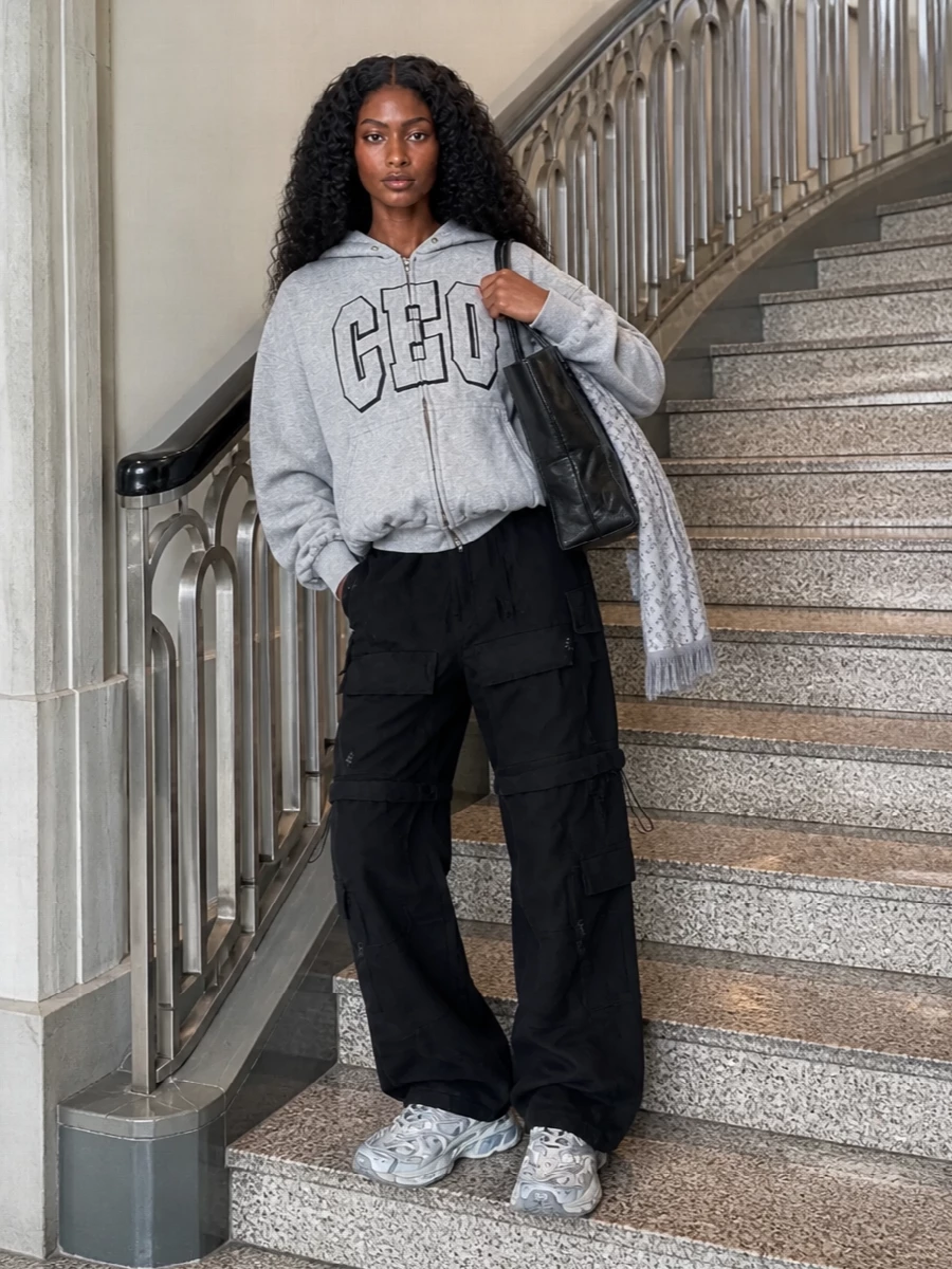 Head-to-toe Balenciaga attitude in a strictly monochrome palette keeps the CEO hoodie feeling tongue-in-cheek rather than literal. The sculpted cargo trouser and hyper-technical grey runner create a strong vertical line, while the oversized leather tote and soft monogram scarf add just enough polish to move from commute to late-night city laps without changing a thing.