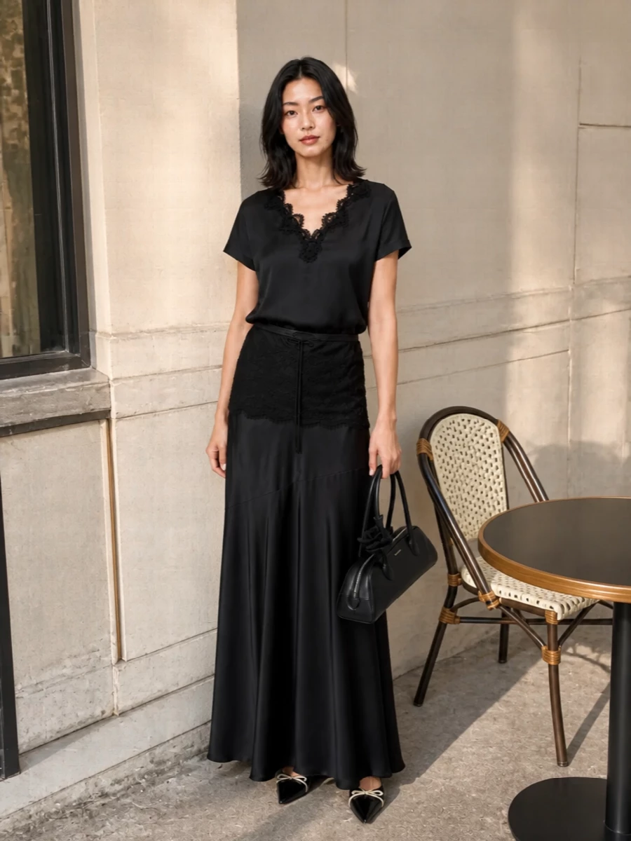 A dark, liquid column of satin and lace runs from neckline to hem, giving this pairing a moody, romantic presence without feeling fussy. The high waist and flared maxi length balance the relaxed tee, creating a long, lean line that works for intimate dinners or at-home evenings that might drift out. Pointed black flats and a sculpted shoulder bag keep everything quiet yet intentional, adding just enough structure to the softness.