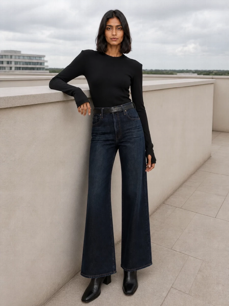 A slim black knit top tucks cleanly into the deep indigo wide-leg jean, keeping the line long and minimal. Block-heel ankle boots and a sculptural brown tote ground the dark palette, while a discreet black belt sharpens the waist and quietly echoes the conceptual edge of the outfit. The result is relaxed but precise, ideal for city days when you want denim to feel intentional rather than casual.