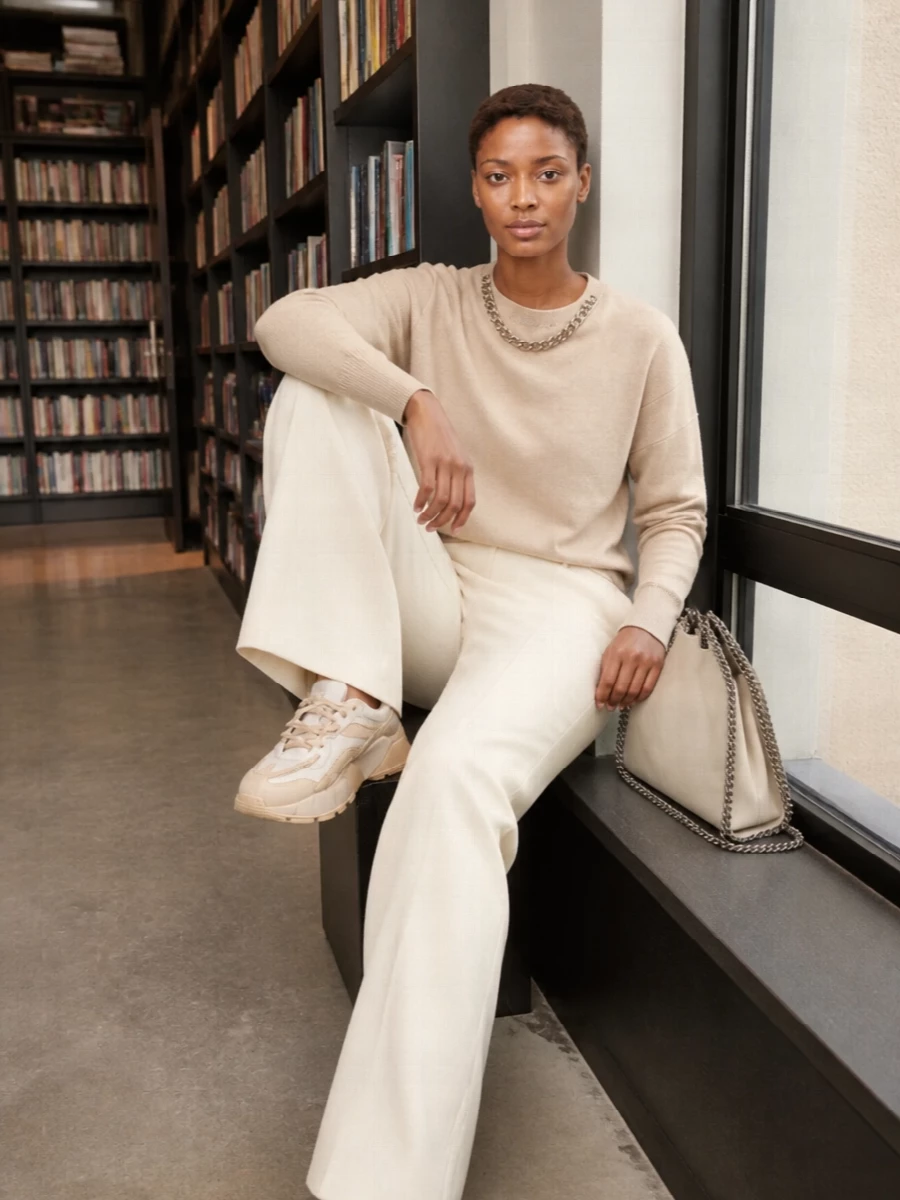 A warm ivory column of wide trousers and a chain-detailed sweatshirt creates an easy, elongated take on quiet luxury. Chunky tonal sneakers keep the energy relaxed and modern, while the silver-chain ivory bag subtly repeats the hardware for a cohesive, considered finish. The result is a soft neutral outfit that moves seamlessly from daytime errands to understated dinners without ever feeling over-styled.