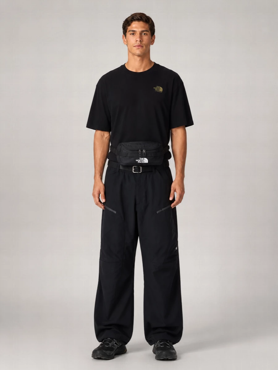 Head-to-toe black keeps this The North Face trouser grounded in a sharp, technical street mood, with the relaxed tee echoing the same easy outdoor energy. The wide leg is anchored by stealthy New Balance trail runners, so the volume reads intentional rather than sloppy. A compact belt bag and clean belt finish it with practical utility that still feels city ready.