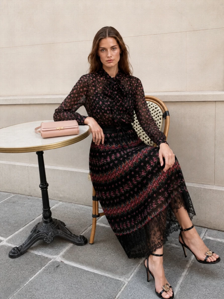 Sheer black florals and a weightless pleated midi create a darkly romantic column that feels soft yet composed. Jewel-detailed black sandals keep the mood cocktail-ready, while blush leather and a delicate printed scarf pick up the rose tones for a quietly sensual finish. It is an Italian garden at night, framed by precise tailoring and a long, fluid line.