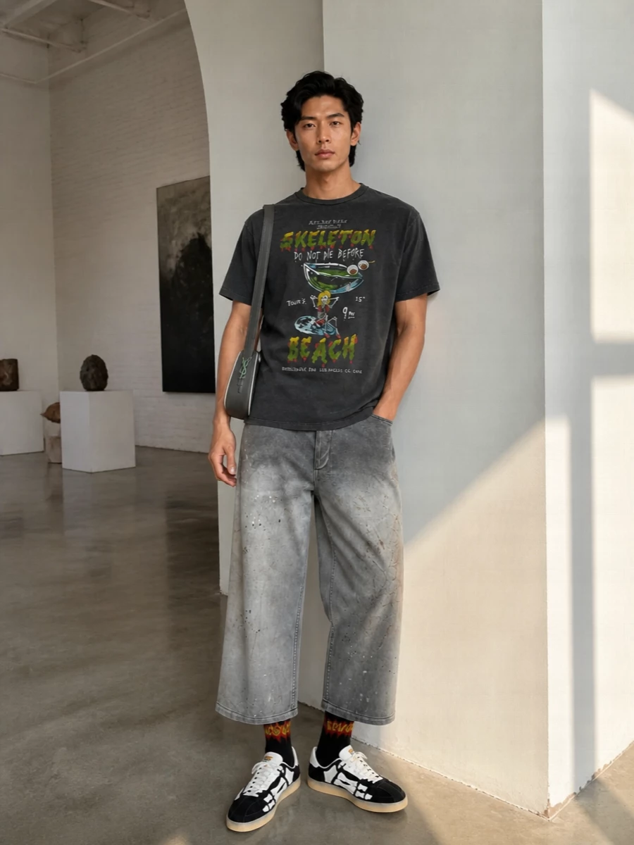 Washed charcoal graphics meet art-damaged wide-leg denim for a streetwear uniform that feels skatey, slightly dark and very LA. The skeleton sneakers double down on the tee’s irreverence, while the charcoal shoulder bag and metal-leaning socks keep the energy graphic but tight. It is relaxed in fit yet intentionally styled, built for all-day city wandering and late-night detours.