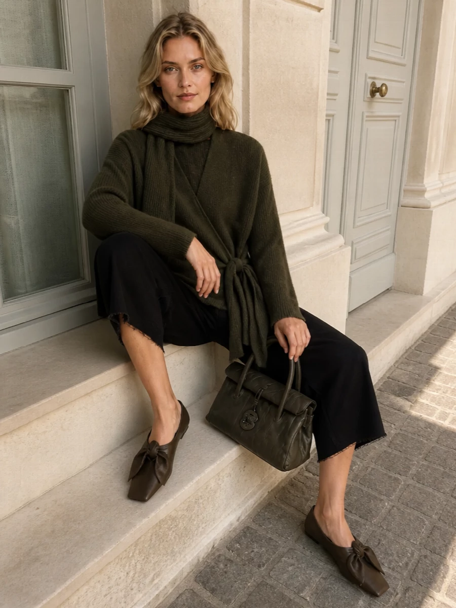 Uma Wang’s wrap cardigan sits against the cropped black wide-leg trouser as a soft, sculptural pairing, all in a deep, moody palette. Sculptural taupe flats and an olive taupe top-handle bag keep the line grounded yet refined, while the dark olive scarf quietly reinforces the cocooned, artful mood. The result is relaxed volume and texture that feel intentional and quietly luxurious for cool weather days and evenings.
