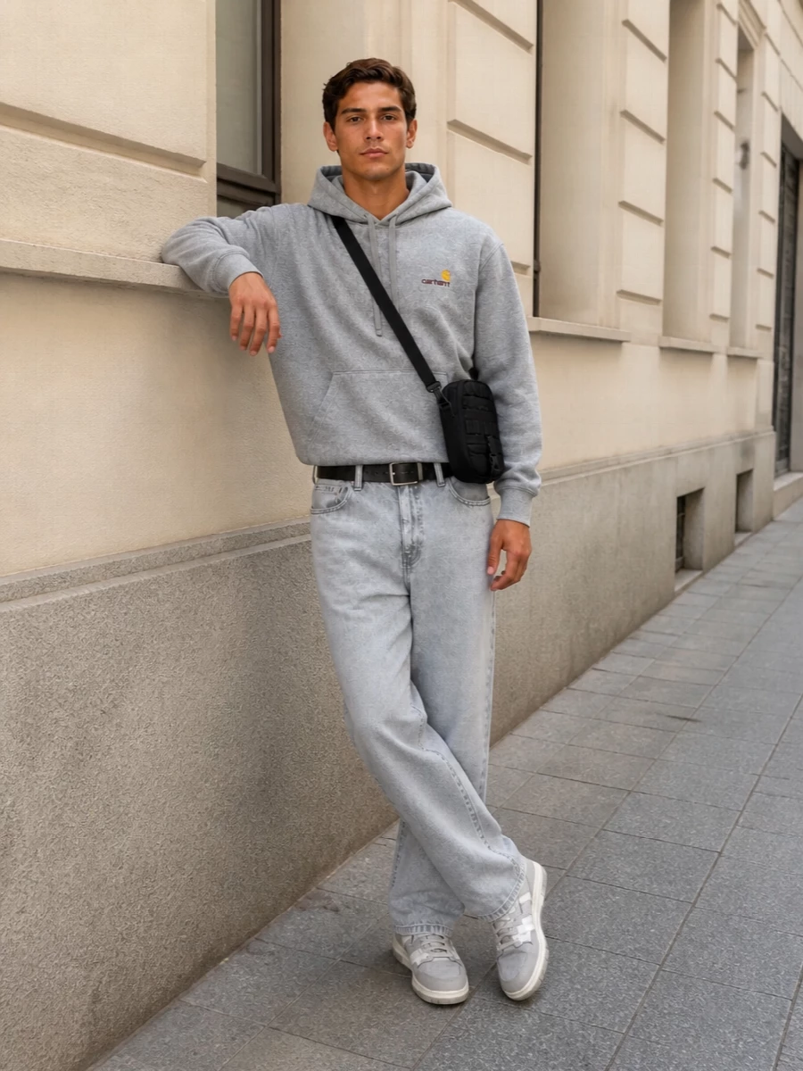A grey-on-grey Carhartt WIP base keeps this outfit tight and calm, letting the small yellow logo hit do the talking. Straight light-wash denim and padded hi-tops sit in that sweet spot between skate and sport, while the compact black crossbody and slim belt bring just enough structure to feel considered without looking styled.