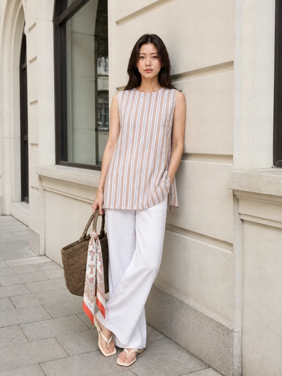 White wide-leg trousers paired with the striped sleeveless tunic create a long, easy column in soft neutrals that moves seamlessly from seaside strolls to city terraces. Cream thong slides keep everything light and modern, while the raffia tote and printed twilly introduce just enough texture and color to feel relaxed but considered.