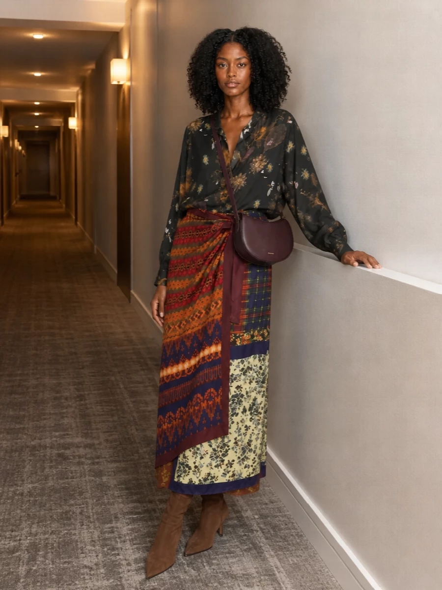 A moody floral shirt in charcoal and mauve leans into the skirt’s folkloric romance without overpowering its patchwork of oxblood, navy and ochre. Sharp chestnut suede ankle boots and a sculpted plum leather cross-body keep the silhouette elongated and polished, grounding all that pattern with a rich, quiet-luxury finish. The result is an autumn-ready mix of dark florals and crafted textures that feels romantic, bohemian and confidently composed.