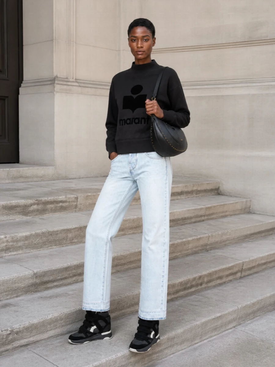 Isabel Marant’s charcoal logo sweatshirt with the icy straight-leg denim creates a clean, laid-back streetwear base that lets the sculpted wedge sneakers stay the focal point. The high rise on the jeans balances the volume of the padded high-tops, while the black studded hobo quietly ties back to the darker tones for a cohesive, city-ready finish. This path keeps the outfit firmly daytime and easy, rather than pushing it into occasion territory the dresses suggest.