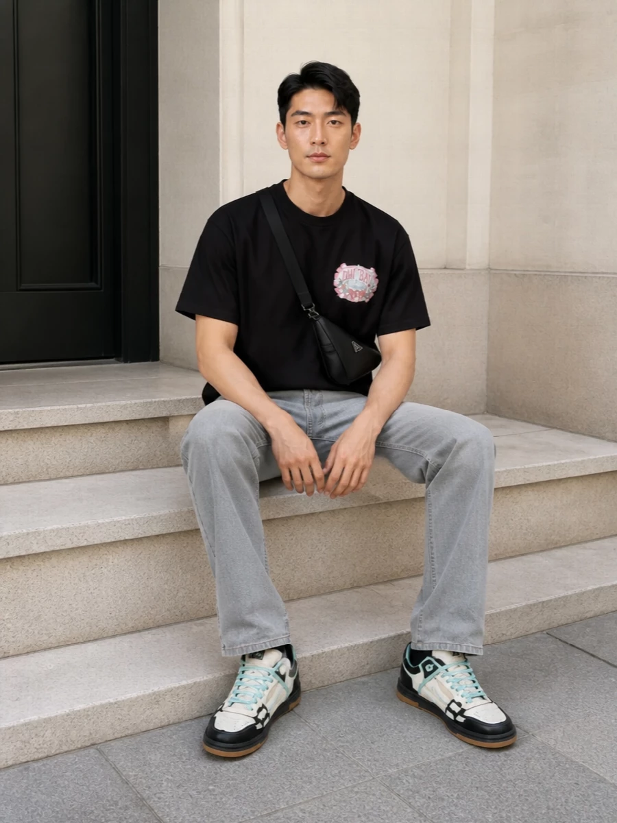 Amiri’s graphic tee sits over straight light-grey denim for a clean, laid-back base that still reads considered. Mint-detailed sneakers pick up the tee’s soft color hits, while the black Prada crossbody and slim belt bring just enough structure and polish to keep the whole mix sharp for city days and late nights alike.