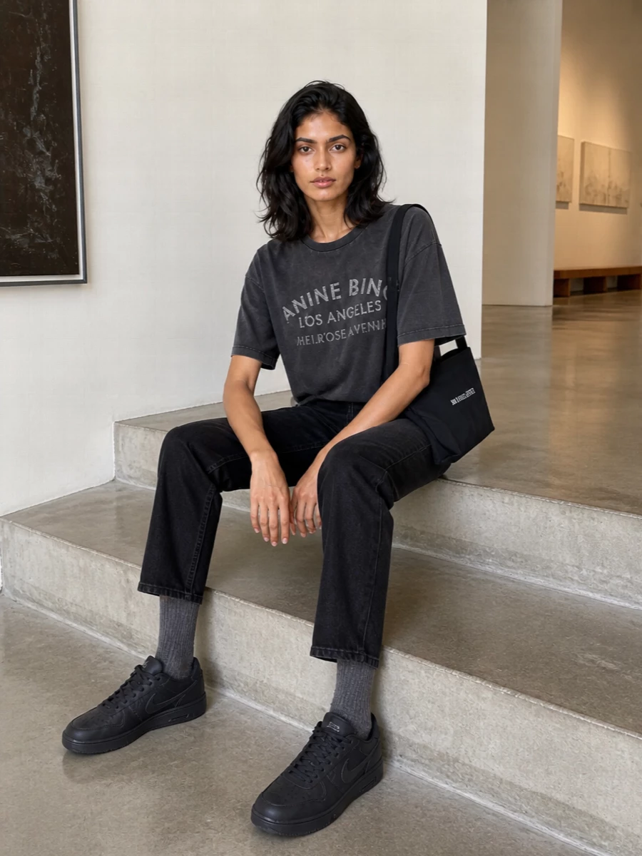 A washed charcoal logo tee, straight faded black denim and tonal black sneakers build an unfussy LA-feeling uniform in a tight monochrome palette. The clean crossbody and subtle logo socks finish it with just enough intention for all-day city wear.