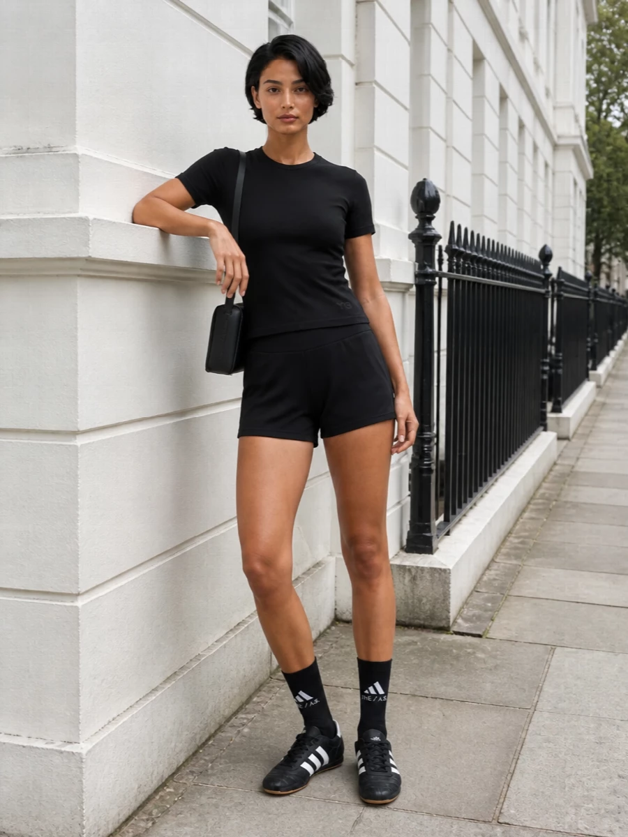 A fitted black Y-3 tee meets a high-rise Alexander Wang sport short for a tight, athletic profile that still reads city ready. Graphic black Adidas low-tops and a slim Alexander Wang shoulder bag keep everything monochrome and intentional, with logoed socks adding just enough detail at the ankle. The result is a sharp, technical-feeling outfit that moves easily from training session to all-day errands without losing its edge.
