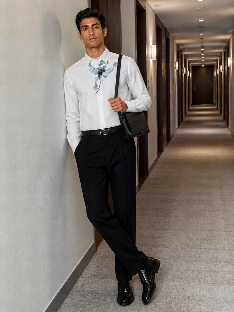 A softly poetic Dries shirt meets precise black pleated tailoring for a romantic yet controlled evening ensemble. The glossy derby and slim black belt sharpen the lines, while the discreet shoulder bag keeps everything composed and city-ready. It is a calm, ink-and-white palette that lets the floral at the chest read as a considered, almost artistic gesture.
