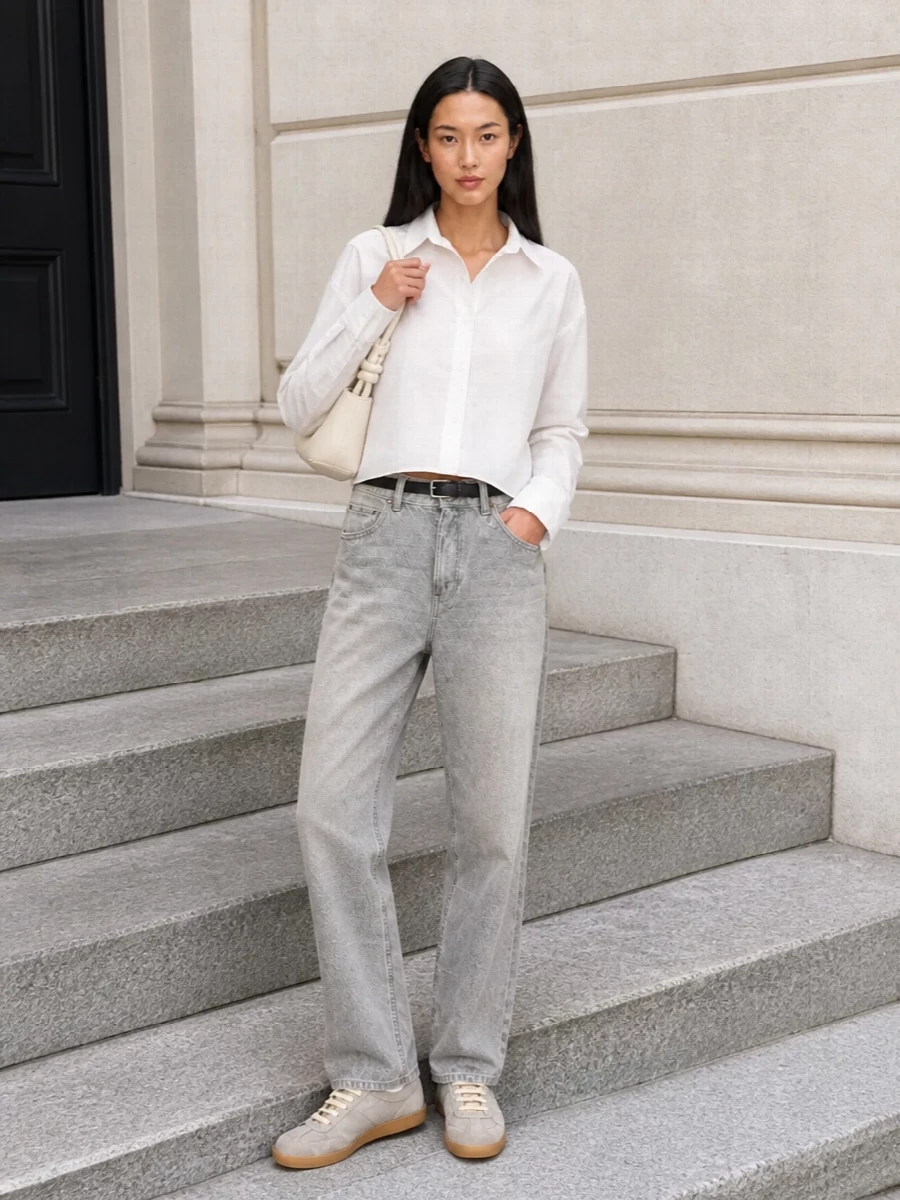 Washed grey Haikure denim meets a sharp cropped white shirt for a clean, modern take on casual tailoring. Grey Margiela sneakers and an ivory Hereu shoulder bag keep everything low-key but considered, with a slim black belt subtly framing the high-rise waist. The result is an easy city ensemble that feels relaxed yet precise in proportion and palette.