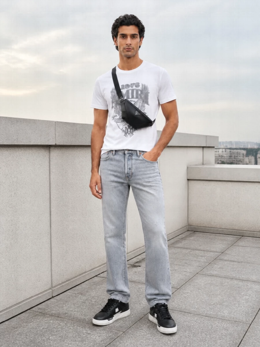A crisp Amiri graphic tee sits on washed light-grey denim, keeping the rock energy sharp but easy for daytime. Chunky black and white sneakers echo the graphics without overwhelming the palette. A sleek black crossbody and clean sport socks finish it with a curated, LA-street feel that still reads pulled together.