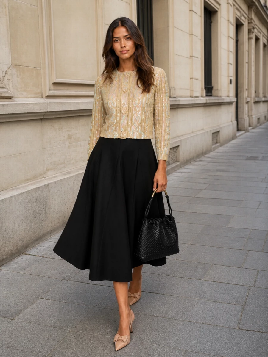 This look pairs the iridescent sand Valentino cardigan with a sculpted black flared midi, creating a romantic, quietly dramatic line that’s perfect for FW cocktail hours and city dinners. Nude-blush slingback stilettos keep the palette soft and leg-lengthening, while a black intrecciato shoulder bag adds artisanal depth and just enough gold hardware to complement the knit’s sequins without overpowering them. The result is polished, feminine, and effortlessly luxurious.