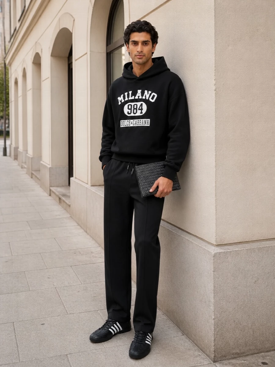 This is a sharp monochrome sport story built around the football-inspired sneaker, with the Milano hoodie and tailored track pants reading like a luxe kit for the city. The straight lines up top and through the leg let the shoe’s texture and stripes do the talking, while the compact logo bag keeps the energy fast and graphic rather than formal.