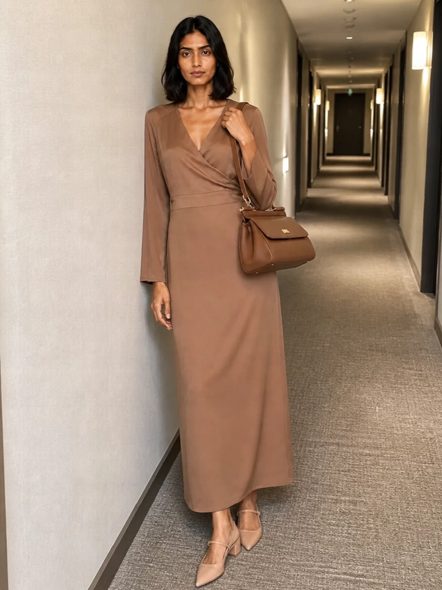 A camel satin wrap dress paired with the structured caramel top-handle bag creates a seamless, tonal column that reads polished without feeling stiff. Nude slingback heels keep the line clean and leg-lengthening, ideal for client dinners or city events where you want tailored ease rather than hard suiting. Choosing the dress route over a full suit lets the bag’s architecture and warm gold hardware quietly take center stage while still feeling impeccably composed.