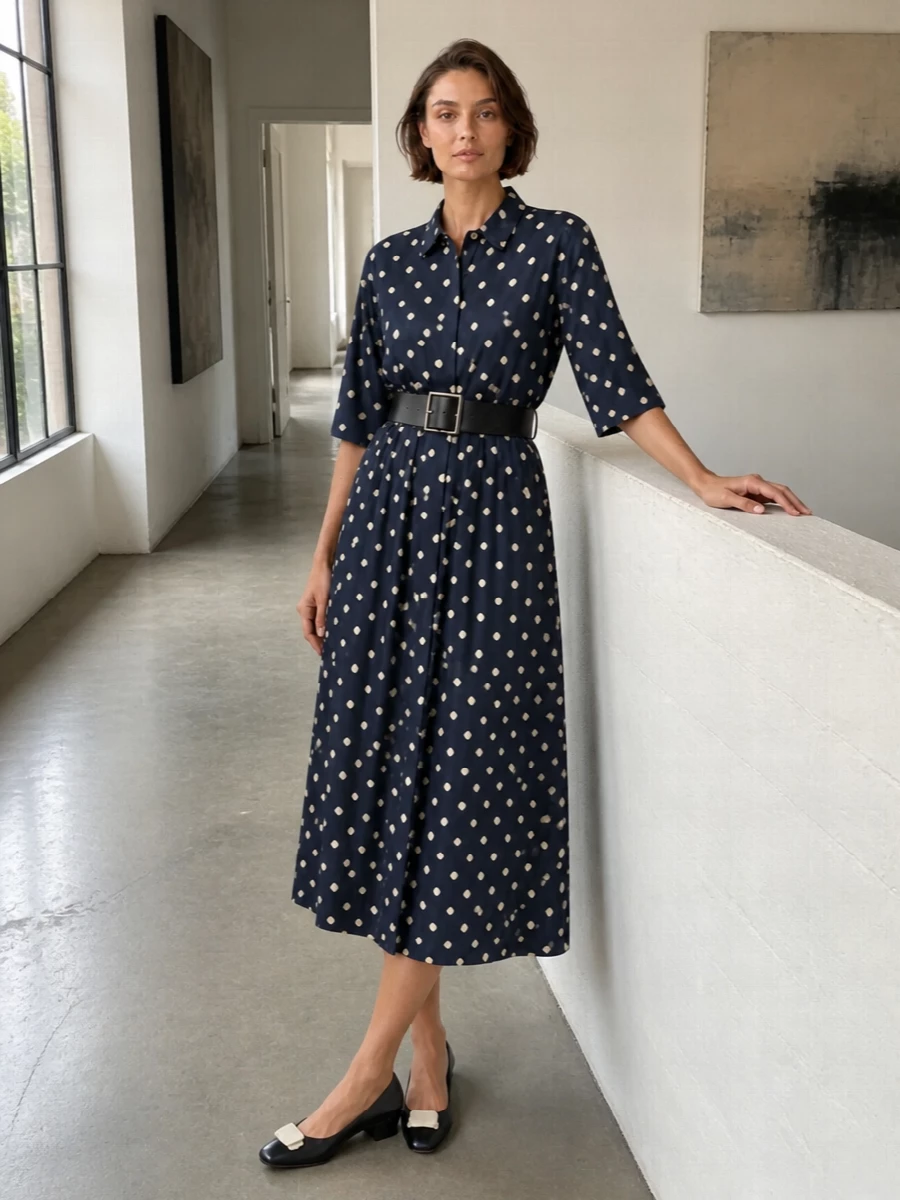 Navy polka dots stay firmly in the modern-preppy camp with a structured mini top-handle and a sleek leather belt sharpening the dress’s soft tie waist. Low-heel navy pumps with a cream accent echo the dots and keep the outfit poised for long city days that drift into dinner. The result is quietly confident and polished without feeling overthought.