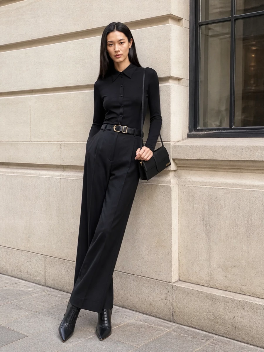 This look is a study in modern tailoring: a sleek black bodysuit shirt disappears seamlessly into the high-waisted wide-leg trouser, letting the elongated, fluid silhouette do the talking. Sculptural pointed ankle boots and a slim black shoulder bag with quiet gold accents sharpen the line further, while a clean black belt subtly carves out the waist for a perfectly balanced, FW-ready uniform that moves effortlessly from gallery night to late dinner.