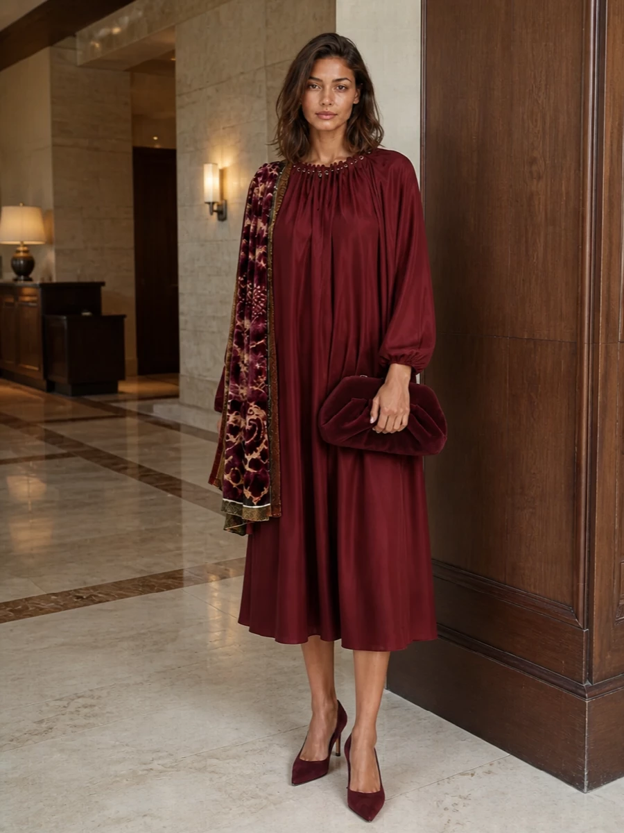 Deep wine and burgundy tones flow from dress to accessories, creating a rich, tonal story with just a whisper of antique gold. Sleek suede pumps and a sculptural clutch sharpen the romance, while the patterned scarf introduces texture and depth without stealing focus from the liquid A-line silhouette.