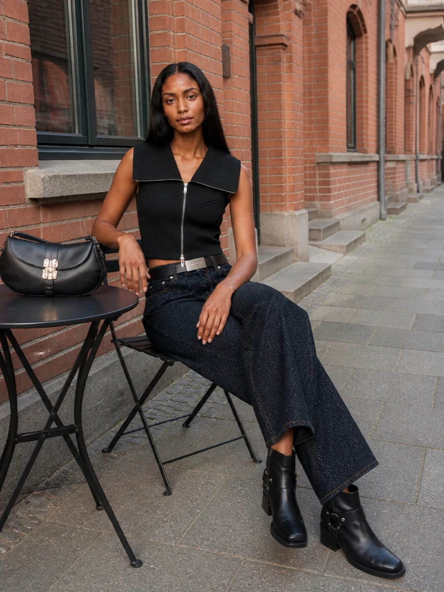 A cropped, sharp black vest sits against deep indigo wide-leg denim for a clean, elongated line with subtle attitude. Harness boots and a structured baguette keep the palette tight and hardware-led, while a slim belt quietly carves out the waist for a confident, modern city outfit. Everything reads minimalist and tailored, with enough edge to move from daytime meetings to low-key drinks without a change.