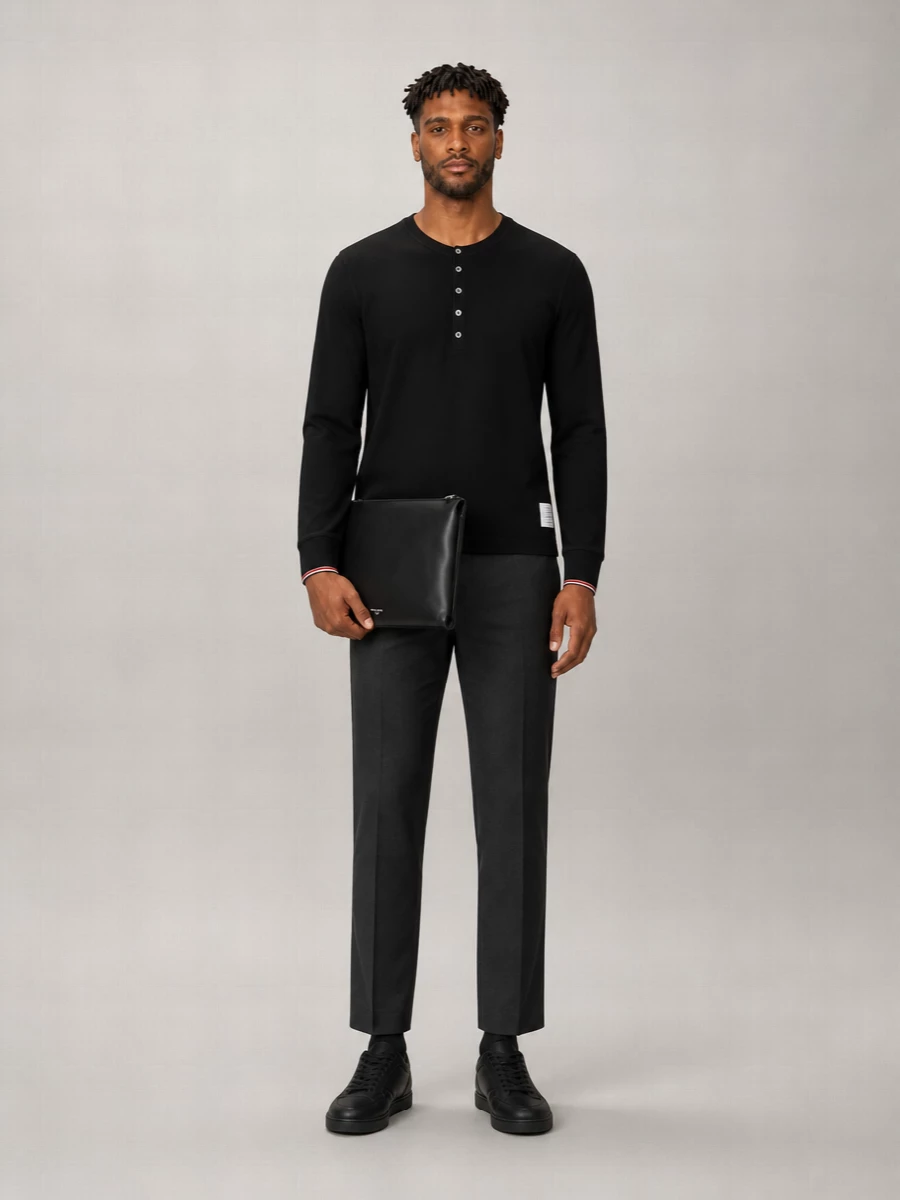A black Thom Browne henley sits against charcoal Dries Van Noten trousers for a calm, tonal take on modern tailoring. Black Louboutin sneakers keep the line sporty but discreet, while a slim Dolce&Gabbana shoulder bag adds just enough structure to read considered without tipping into full suiting. The result is a quietly luxurious uniform for city days that stretch into dinner.