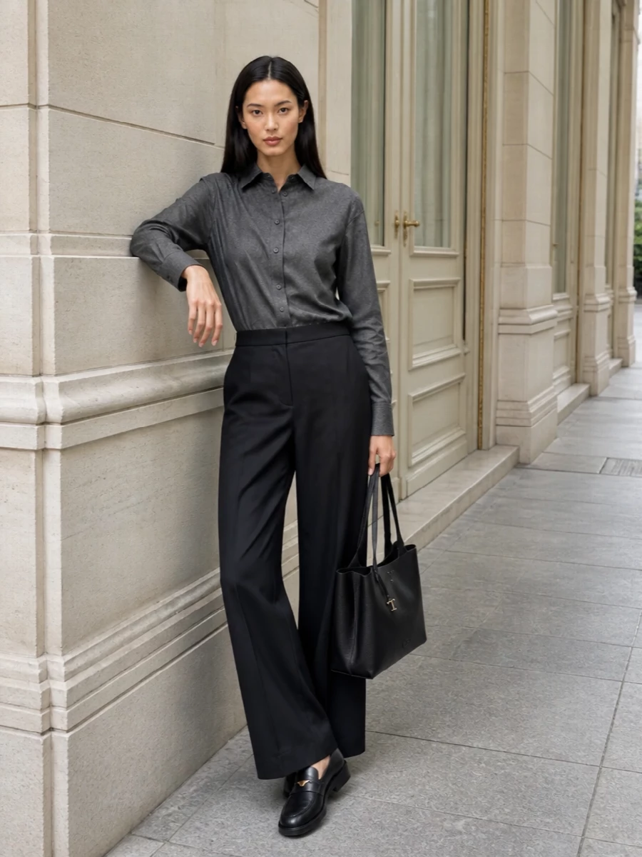 A charcoal wool shirt tucked into deep-charcoal wide-leg trousers creates a long, uninterrupted column that feels precise yet relaxed enough for full days in the city. The structured black tote and square-toe loafers add a subtle boardroom edge, reading as quiet authority rather than overtly corporate. This path keeps everything tailored and tonal, aligning the outfit with the bag’s travel-meets-office intent while remaining understated and modern.