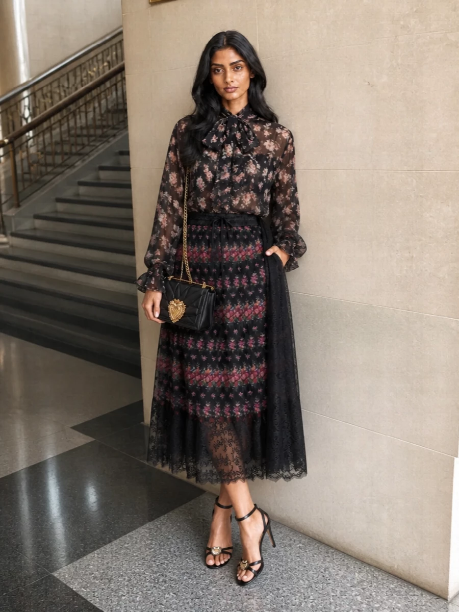Dolce&Gabbana’s pleated floral skirt meets a sheer pussy-bow blouse to create one continuous, darkly romantic rose garden for summer evenings. Strappy jeweled black sandals and a quilted Devotion bag sharpen the mood, keeping the silhouette light, leggy and unmistakably Italian for cocktail hours and dinner dates alike.