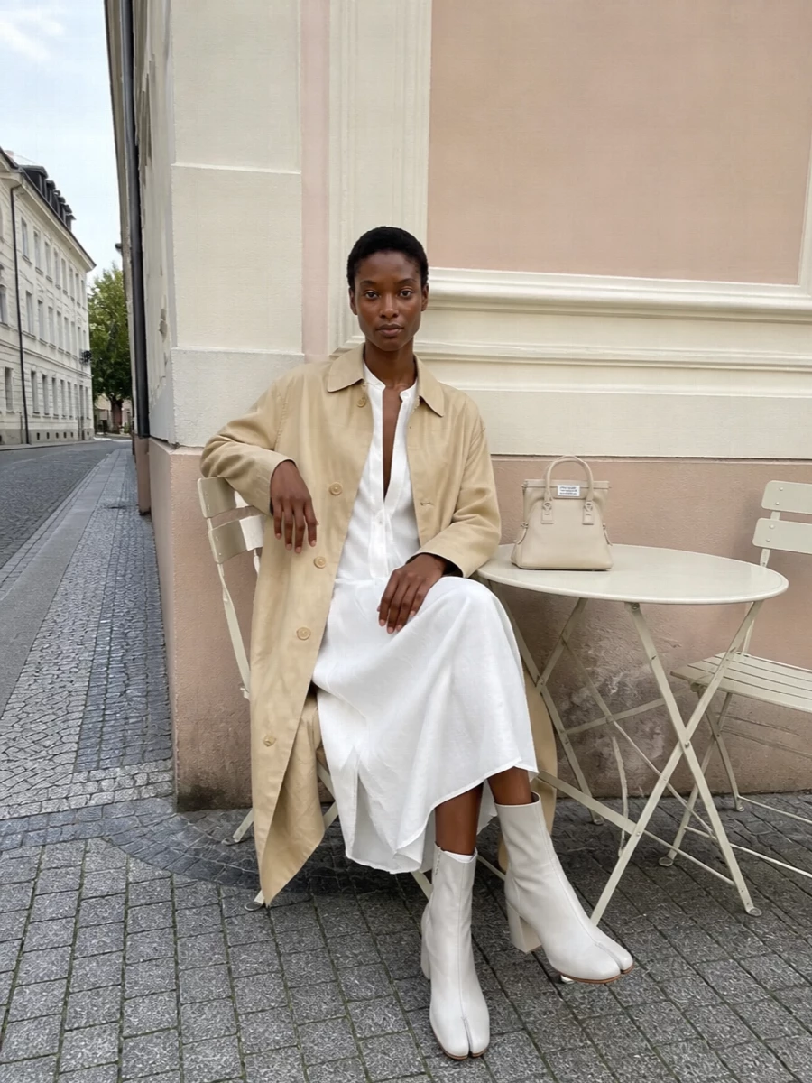 I’ve taken the trench away from denim cut-offs and into a cleaner Margiela uniform, with a long white shirt dress underneath so the lines stay sharp and relaxed rather than busy. Light-grey Tabi boots and a structured cream mini bag keep the palette calm and the silhouette columnar, giving you quiet drama that works from daytime appointments to low-key dinners. I chose the dress route over tailoring separates to preserve that uninterrupted vertical line the coat loves and to lean into the house’s signature shirt-dress language.