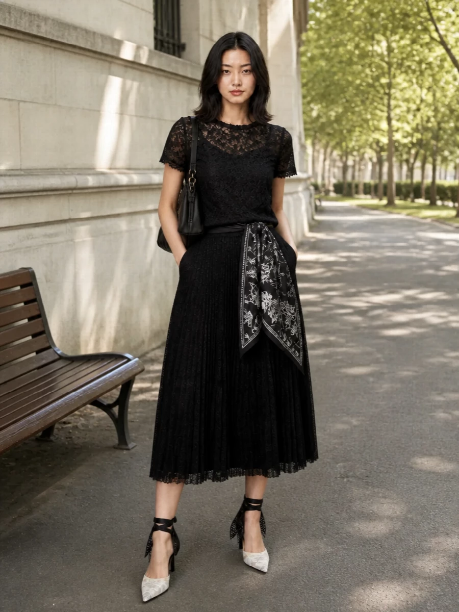 A study in noir romance, this outfit layers sheer black lace with a matching pleated midi to create a fluid, softly structured silhouette. Lace ankle-strap stilettos and a ruched black shoulder bag keep the mood firmly in the cocktail hour, while a subtle patterned scarf adds just enough detail without disturbing the quiet refinement. The result is evening dressing that feels light, modern and intimately considered.