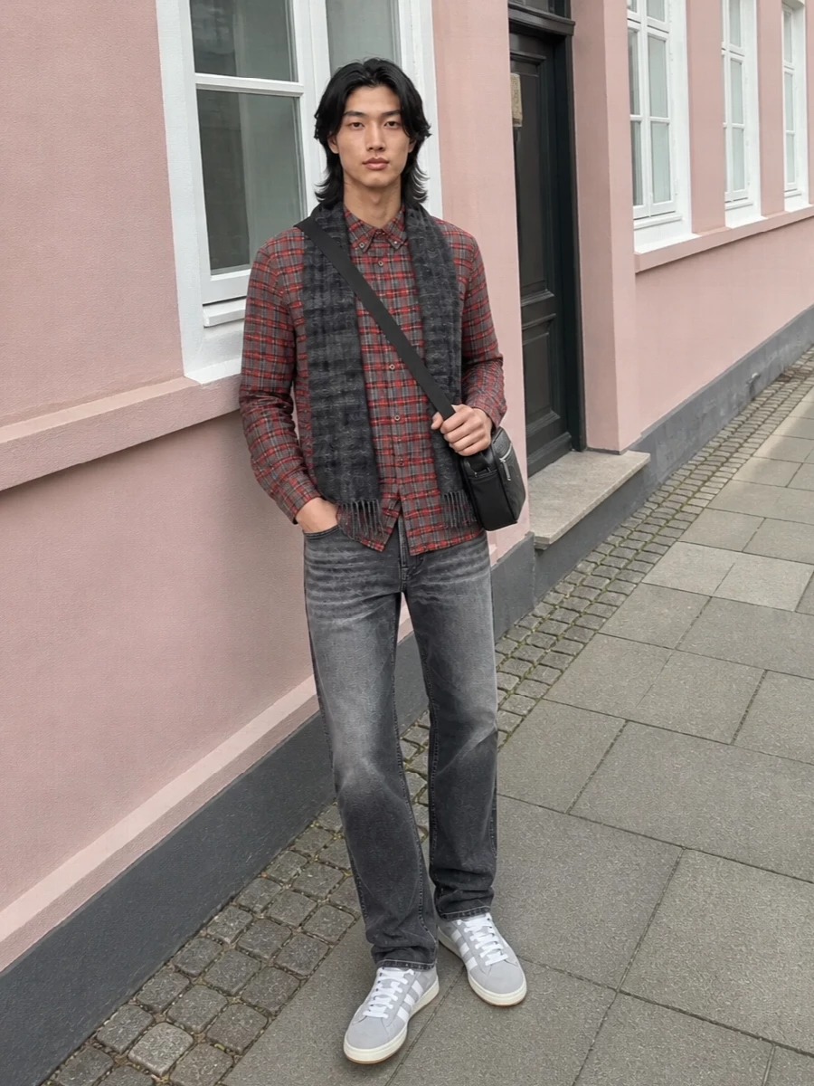 Charcoal-wash denim and a brushed red check shirt keep this firmly in that 90s-leaning grunge-prep space without feeling heavy. Light grey suede sneakers and a tonal black crossbody sharpen it just enough for city days, while the soft grey scarf adds warmth and subtle pattern play. The result is relaxed, layered and coherent in a tight red, charcoal and grey palette.