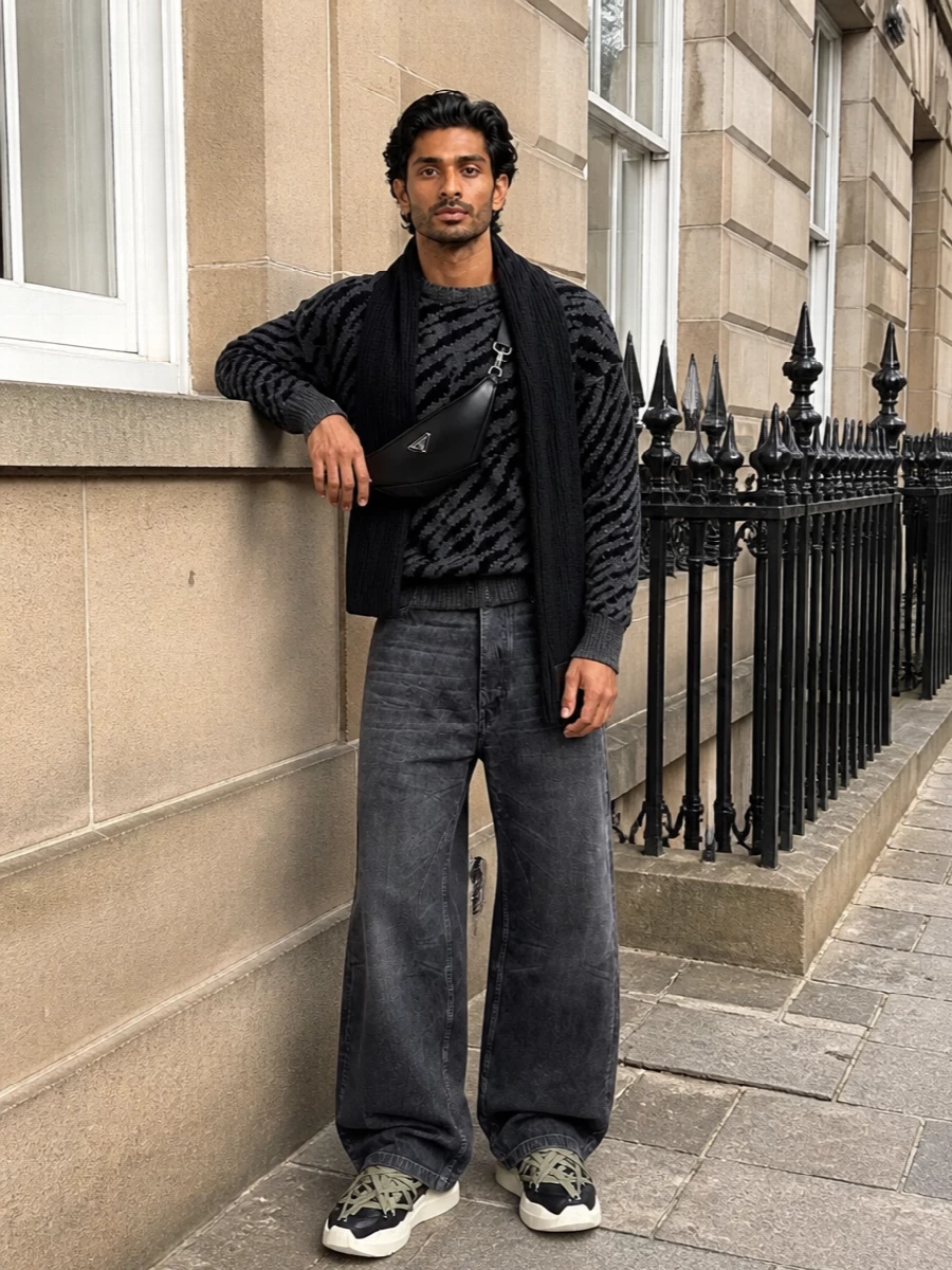 Rhude’s distressed zebra knit sits over loose Rick Owens charcoal denim for a monochrome, grunge-lean street take that still feels considered. Chunky high-top sneakers keep the proportions grounded, while a technical Prada crossbody and ribbed scarf bring a precise, city-ready finish in the same shadowy palette.