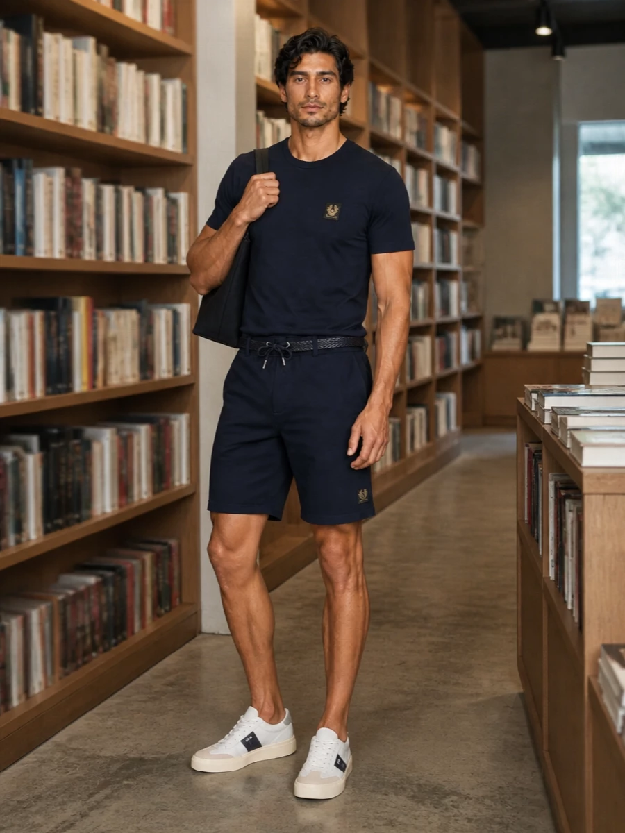 A navy-on-navy base keeps the outfit clean and calm, with the Belstaff tee and matching shorts reading as a single, intentional set rather than gymwear. Off-white court sneakers soften the palette and stay sporty without noise, while the navy tote and braided belt bring just enough structure for city days or relaxed travel. The result is minimal, coherent and quietly functional from morning errands to late-afternoon drinks.