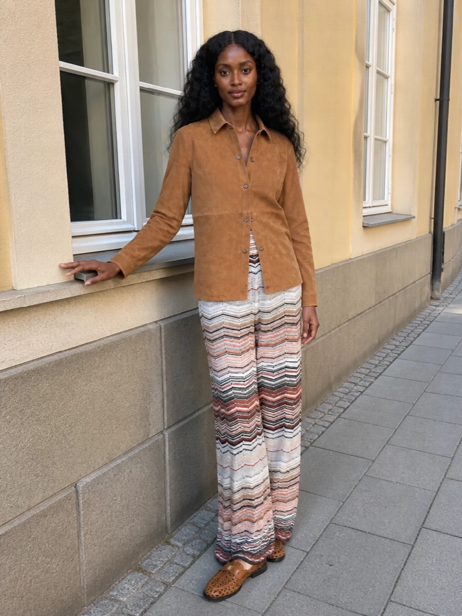 This outfit leans into a sun-warmed boho mood anchored in quiet luxury, pairing the camel suede shirt with fluid Missoni chevron trousers that echo the loafers’ artisanal texture. The high-rise wide leg balances the relaxed shirt, while the natural raffia-and-leather tote completes a cohesive palette of cognac, camel and soft neutrals. Choosing the top-and-trouser route here keeps the silhouette long, easy and versatile, which suits the woven loafers better than the more structured dress options would.