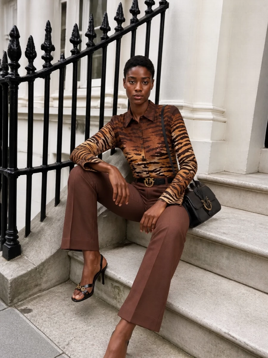 Pinko’s tiger-print shirt becomes the hero against clean chocolate tailoring, pulling all that print energy into a long, lean line. Strappy black heels, a structured cross-body and a fine gold-detailed belt keep the mood nightlife-ready but controlled, letting the pattern move while the silhouette stays sharp. It is the kind of brown-and-black mix that feels intentionally glam rather than casual, perfect for city evenings and parties where you want impact without fuss.