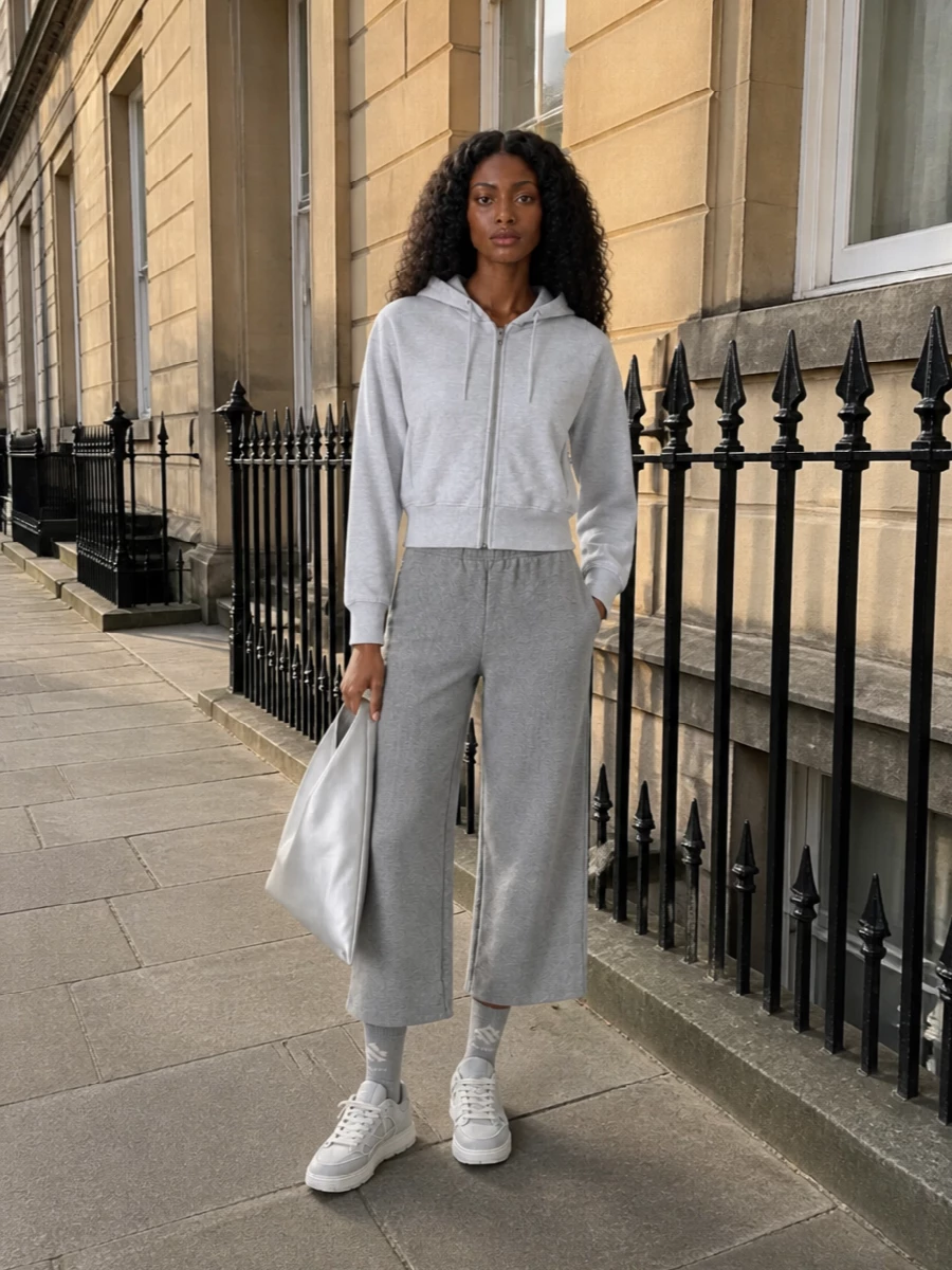 Head-to-toe grey feels intentional here, with the cropped hoodie and wide-leg sweat pulling together into a relaxed, quietly graphic set. Tonal padded sneakers and a sculptural silver hobo keep the mood modern and city-ready. Soft logo socks are the only visible branding, so the whole outfit stays calm, directional and easy to live in all day.