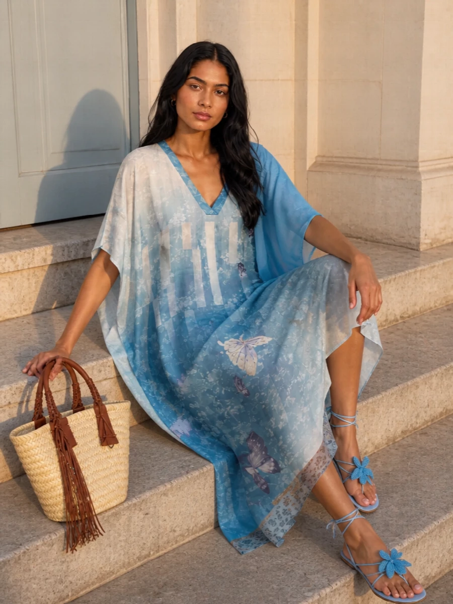 A washed-sky kaftan, powder blue sandals and a woven straw tote create a soft-focus, beach-to-terrace ensemble that feels poetic rather than prim. The palette stays in sun-faded blues and warm sand tones, so every element whispers of sea and driftwood. A sheer sky wrap is your lightweight layer when the sun drops but you want to keep the mood dreamy and undone.