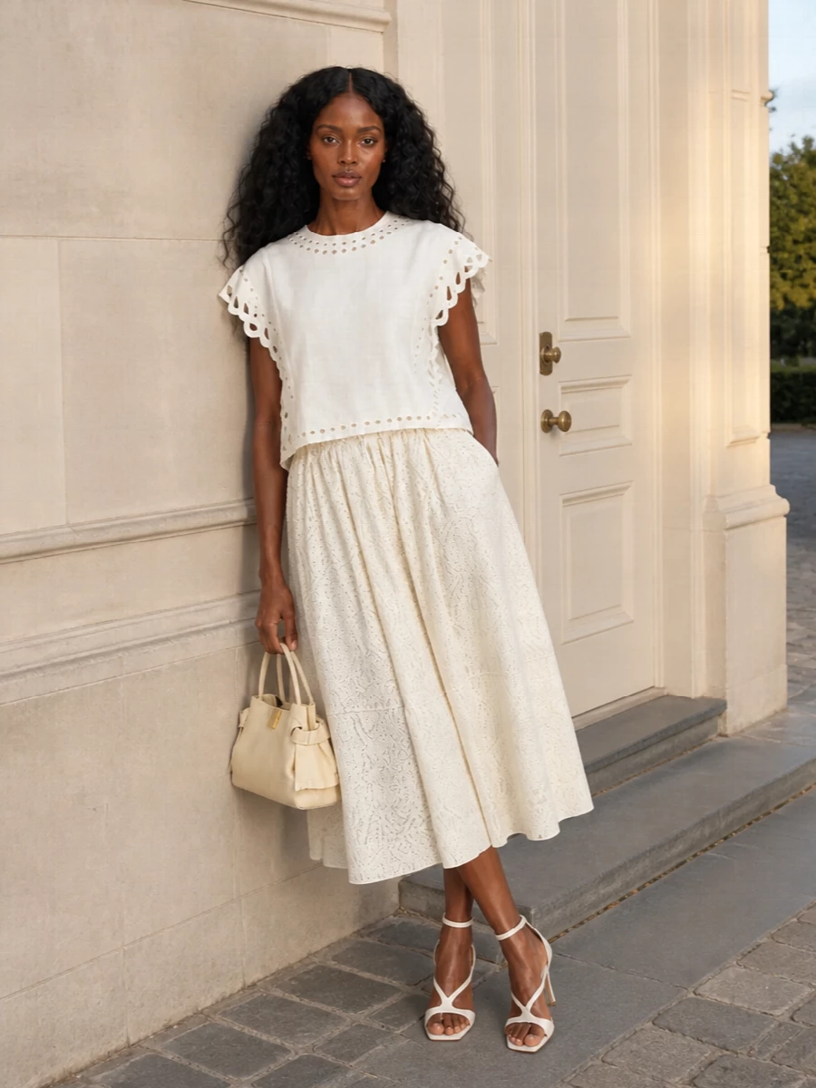 An ivory-on-ivory story that leans into texture, pairing the eyelet blouse with a full lace midi for soft movement and quiet romance. Strappy ivory heels and a buttercream top-handle bag keep the mood polished yet easy, ideal for warm city days that slip into dinner. The result feels feminine and bohemian, but held in a clean, modern palette.