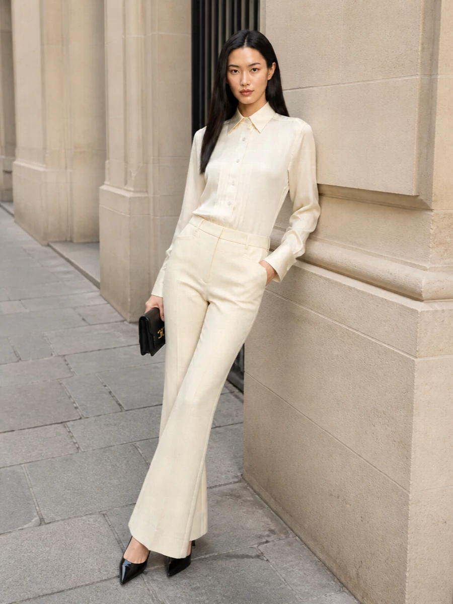 The buttercream tuxedo shirt is paired with matching flared Tom Ford trousers to create a luminous, elongated column of soft neutrals that feels refined yet sensual. Black patent d’Orsay pumps and a compact black flap bag cut through the light palette, adding just enough contrast and gloss to keep the look sharp, evening-leaning, and impeccably minimalist.