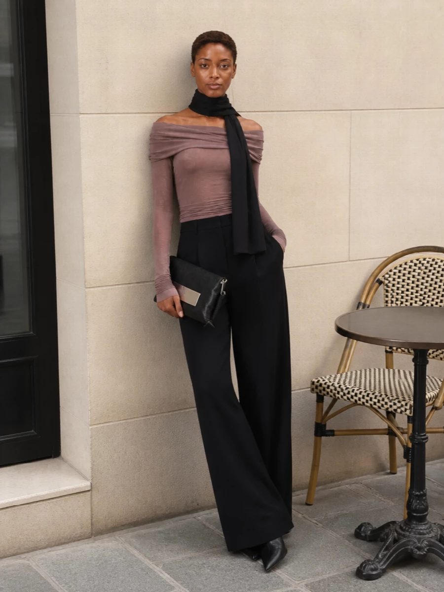 Rick’s mauve taupe off-shoulder mini is treated as a fluid top, disappearing seamlessly into high-waisted black wide-leg trousers for a long, graphic column. Sculptural pointed boots continue the line under the hem, while a compact black clutch and inky scarf add just enough texture and hardware to keep the mood dark, minimal and quietly sensual for night.