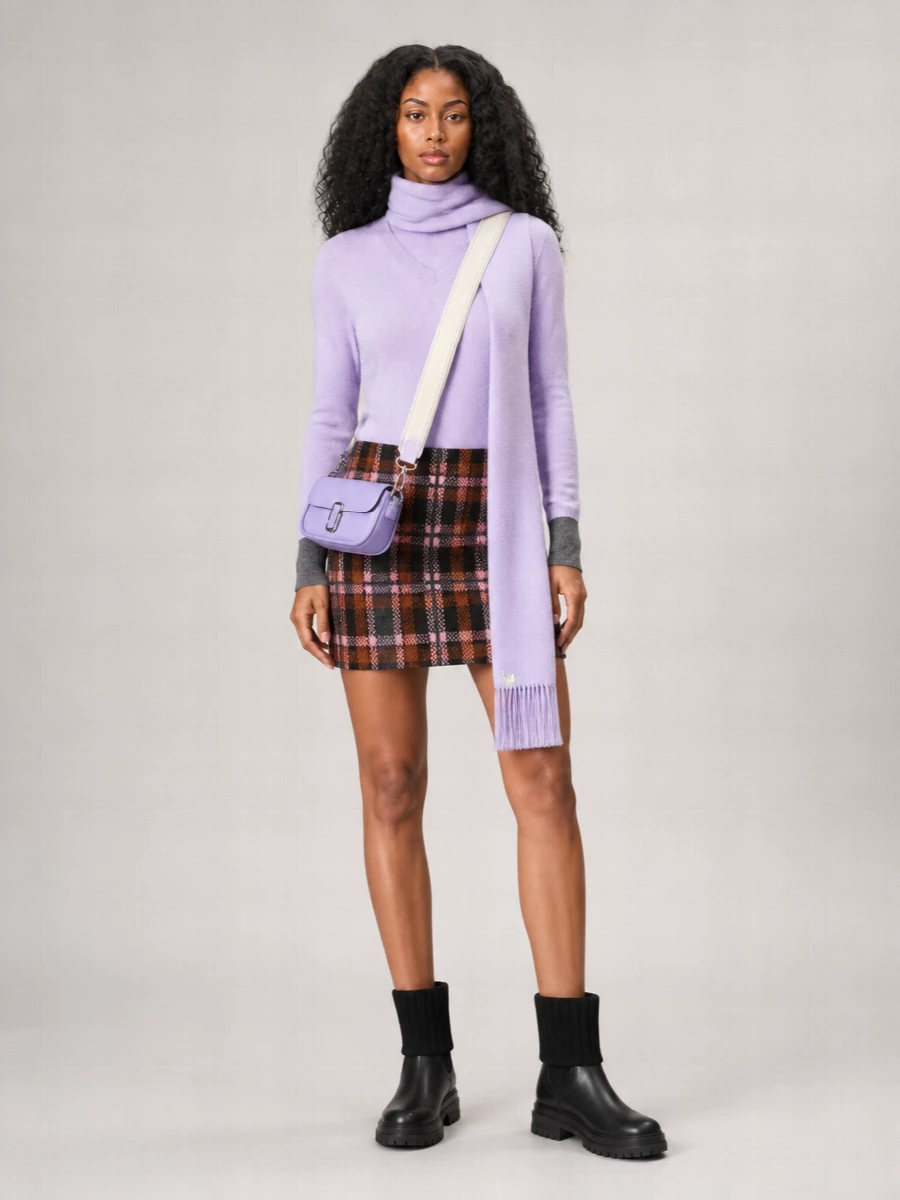 A lilac Marc Jacobs knit meets a collegiate plaid mini for a street-smart, preppy winter pairing grounded in charcoal and soft pink. Chunky black ankle boots give the proportions weight and edge, while a lilac cross-body and slender matching scarf stitch the color story together without feeling saccharine. It is cozy enough for off-duty days yet sharp enough for casual city evenings.