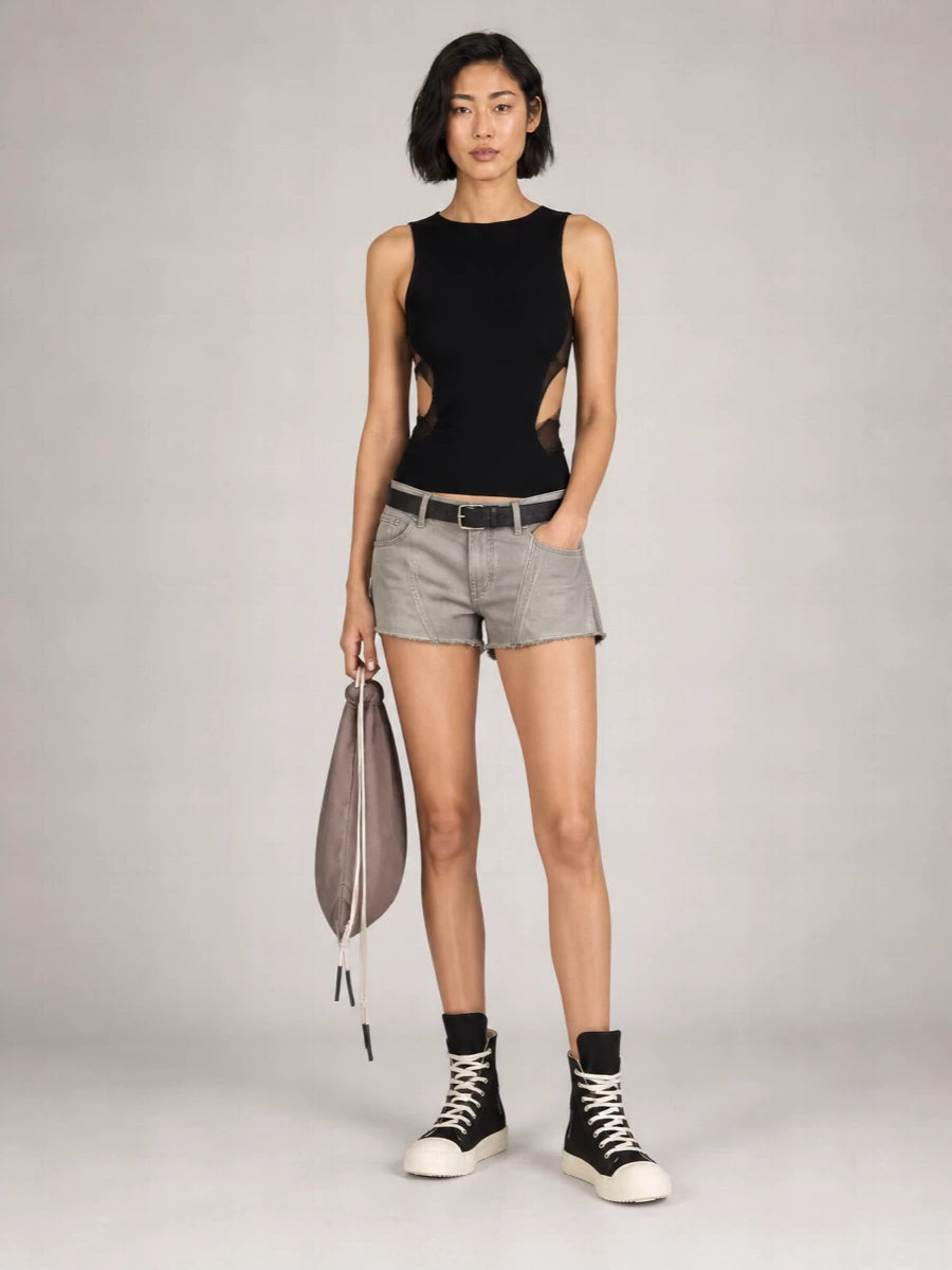 DRKSHDW’s mid-rise frayed shorts meet a razor-cut black tank for a dark, skin-baring city uniform that still feels grounded and utilitarian. Chunky high-top sneakers keep the energy street and practical, while a muted taupe drawstring backpack and slim black belt add quiet structure and function without diluting the dystopian edge.