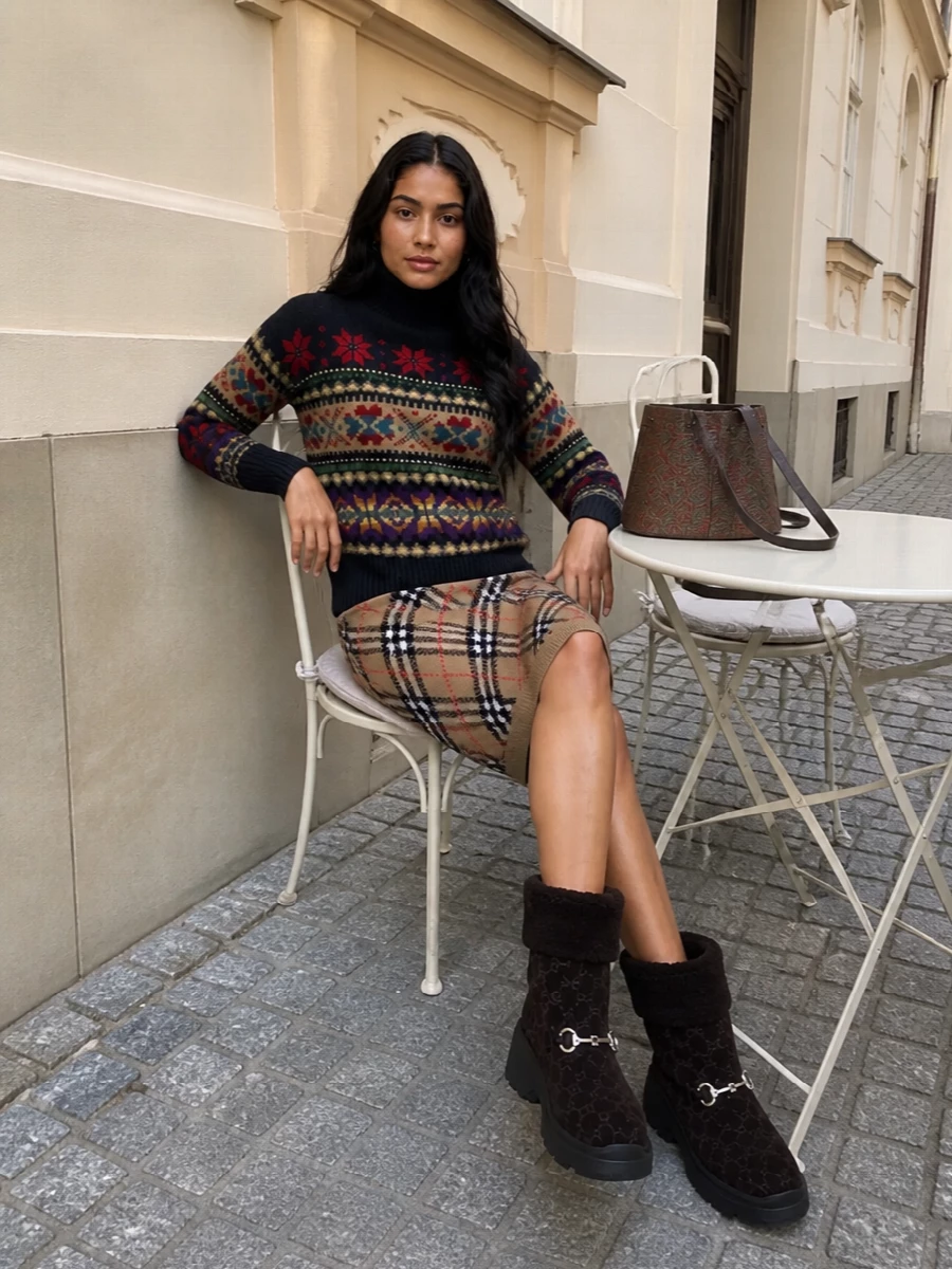 An inky Fair Isle knit is anchored with a camel argyle skirt for a rich, heritage spin that still feels easy for daytime. Deep chocolate shearling boots ground the colour story, while an Etro paisley bucket and a soft neutral check scarf introduce a subtle boho layer that plays quietly with the sweater’s pattern. The result is a cozy, chalet-ready ensemble that still reads considered enough for city errands or weekend lunches.