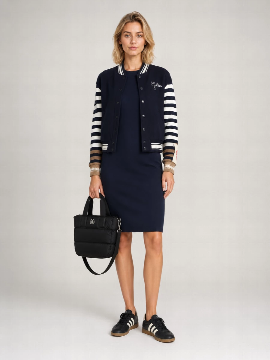 I’m anchoring this with the Max Mara striped-sleeve knit dress rather than separates, because its navy body and collegiate stripes speak fluently to the Golden Goose varsity jacket without feeling try-hard. Black and cream Adidas sneakers and the padded Moncler mini tote keep the story in that sport-preppy space, with textures and subtle branding doing the work instead of extra color. The result is a polished, city-ready take on campus style that feels confident rather than nostalgic cosplay.