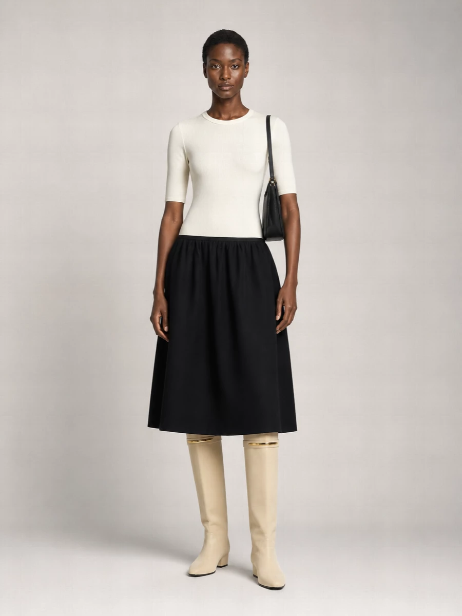 A two-tone Totême midi sets a precise black-and-ivory column that lets the buttercream Givenchy boot read as a sculptural statement rather than competing for attention. The asymmetric palette stays within a tight neutral story, so the gold flash at the boot and hardware on the Alaïa bag feel like deliberate punctuation instead of ornament. Choosing the dress route keeps the outfit quietly formal and streamlined, ideal for refined evenings where proportion and restraint do the work.