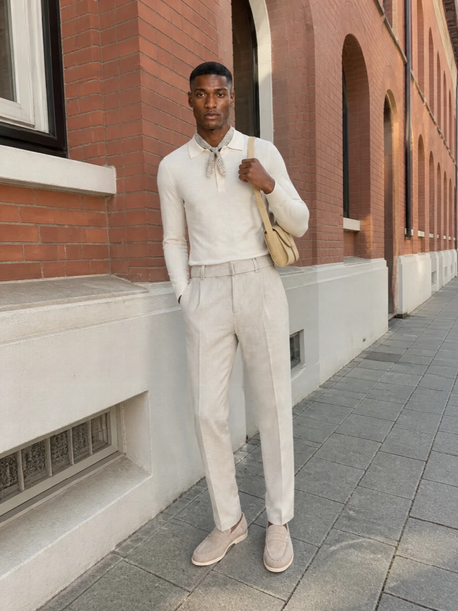An ivory knit polo sits cleanly above light‑beige pleated trousers for a tonal, tailored take on warm‑weather dressing. Pale stone suede loafers keep the line refined yet relaxed, while a slim buttercream shoulder bag and a small geometric scarf add just enough structure and detail. The result is quietly polished, ideal for city days that drift into dinner on a soft summer evening.